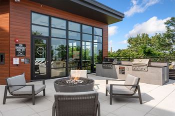 a patio with chairs and a fire pit in front of a building with large windows